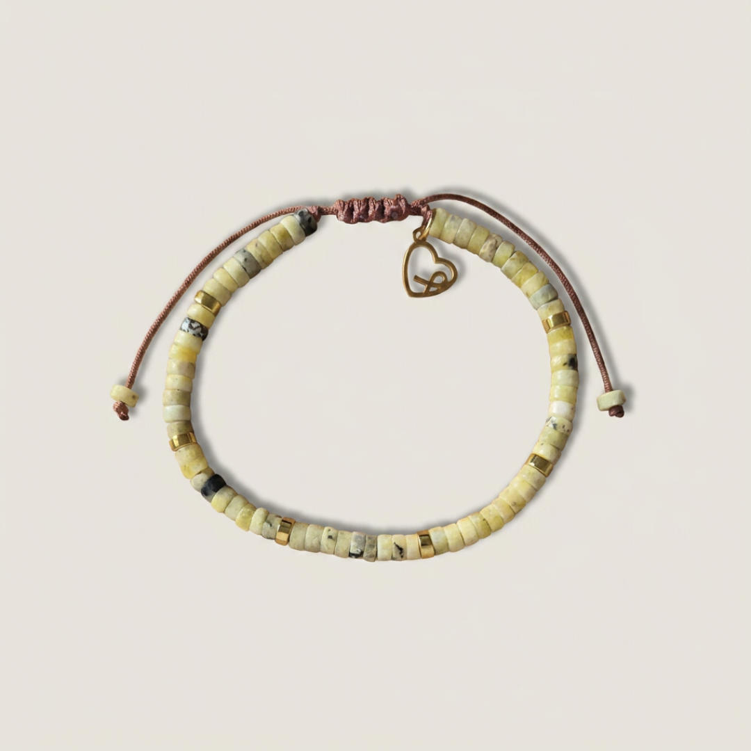 Pulsera Cabrera con cuentas de crisoprasa verde limón, separadores dorados, cordón de macramé marrón ajustable y dije de lazo solidario en acero inoxidable dorado, sobre fondo neutro.